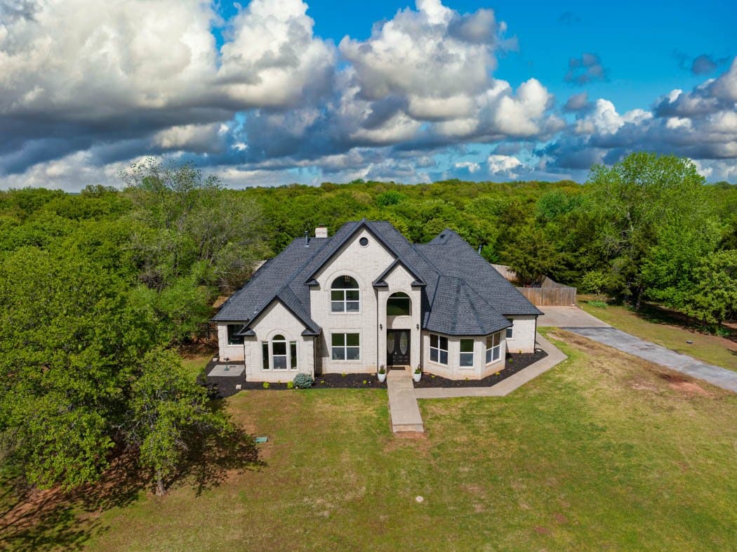 Aerial view of a brick two-storey home on a wooded acre lot