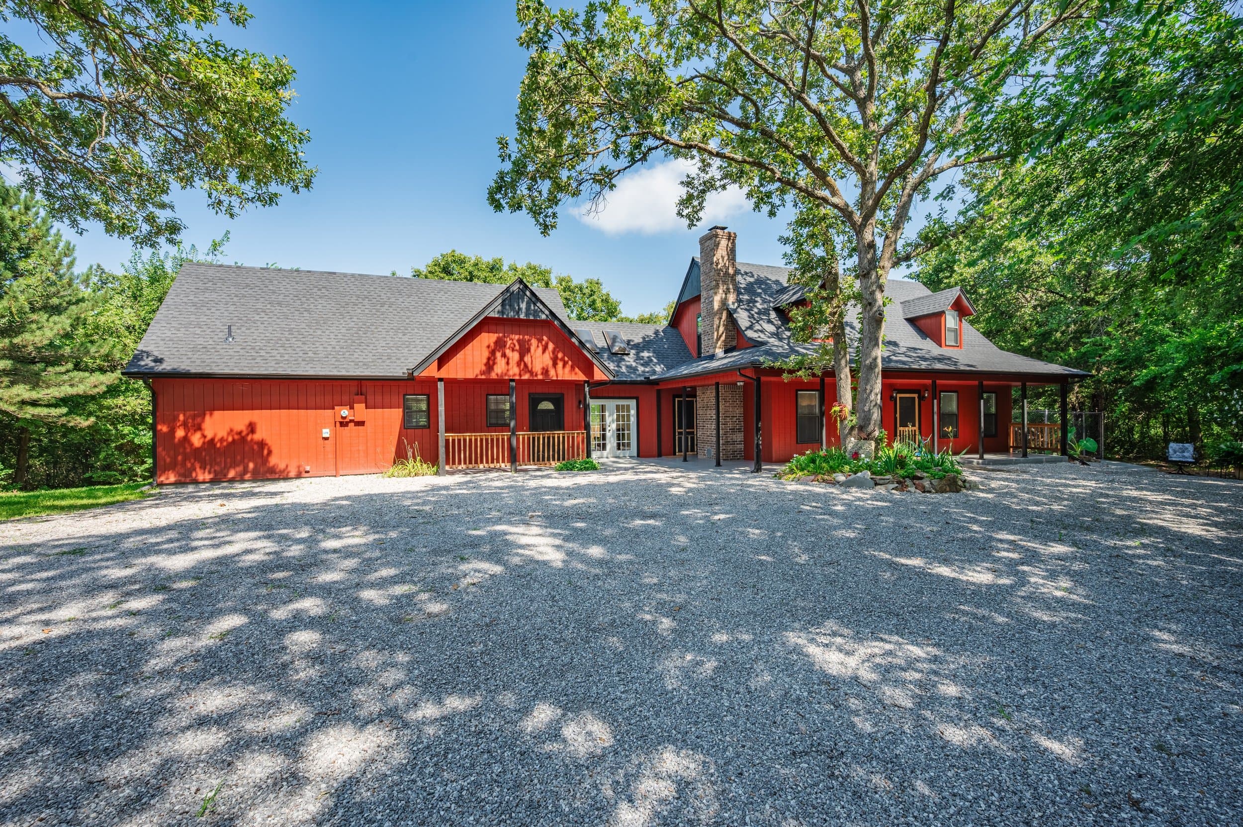 Barn-red country home with a wraparound porch under mature oaks