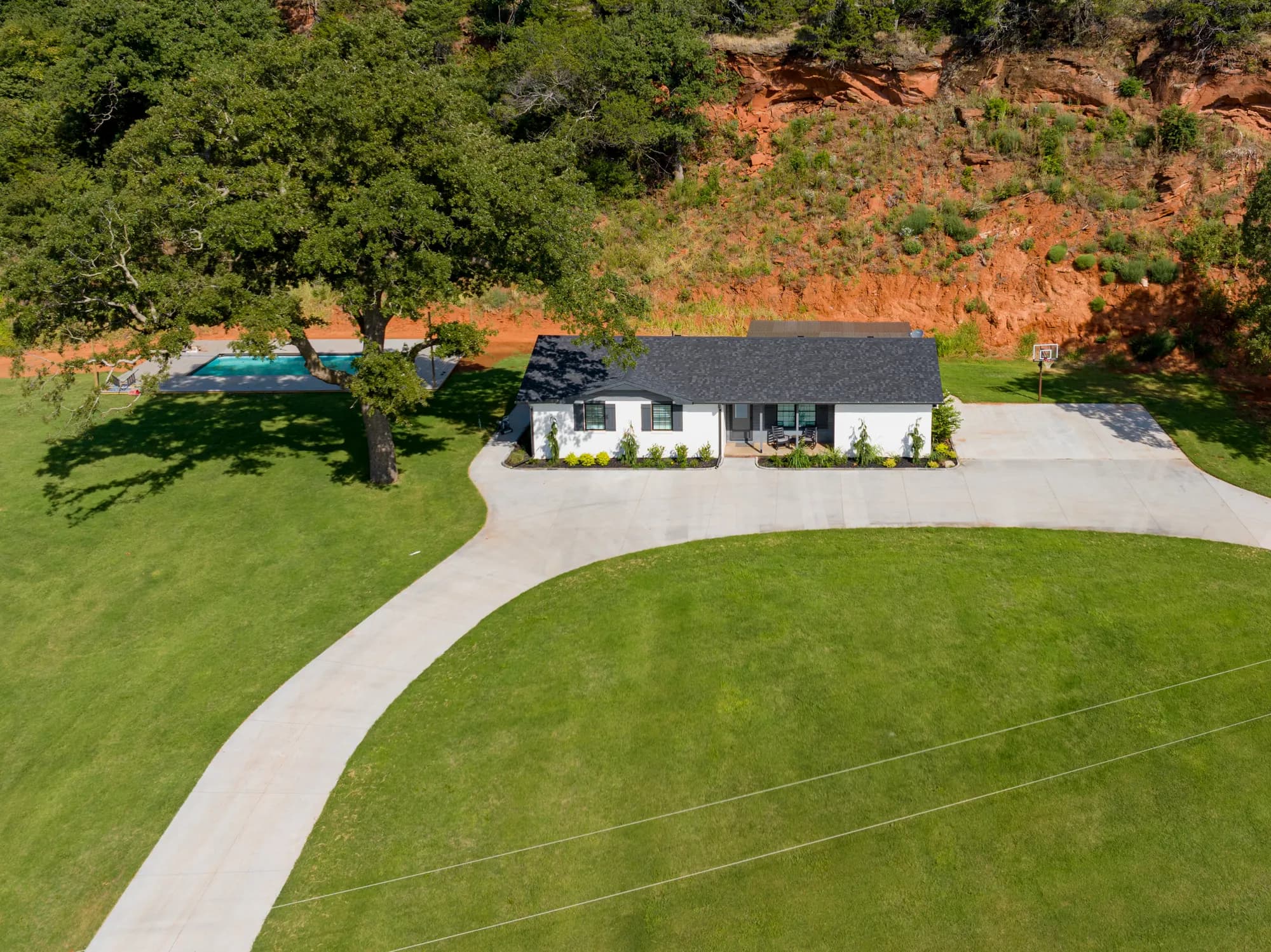 Aerial view of a ranch home and pool set against a red rock bluff