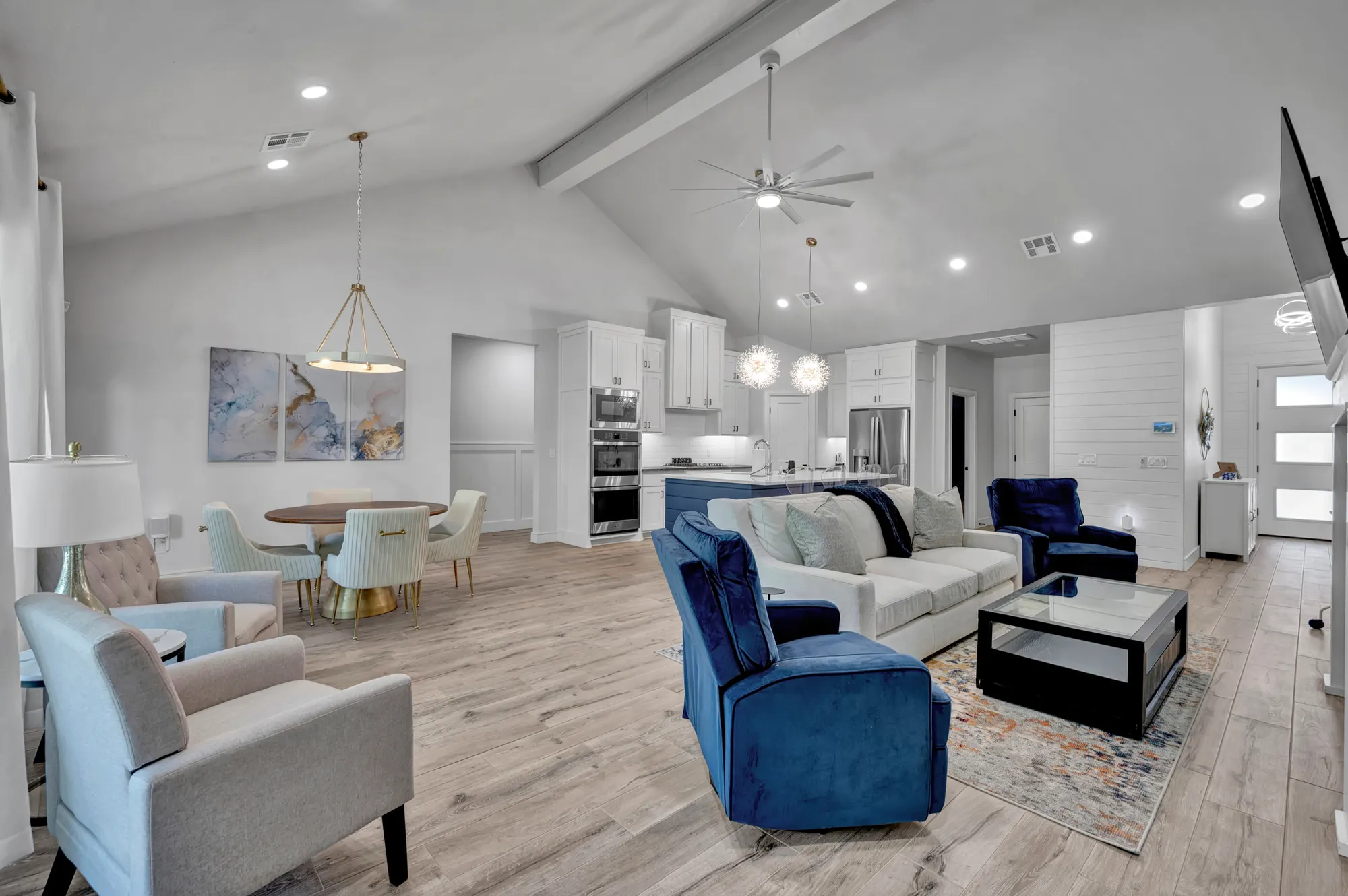 Open living and dining space with blue velvet sofas and a wood-beamed ceiling